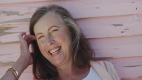 Portrait-of-happy-senior-caucasian-woman-laughing-by-weathered-pink-wooden-wall,-in-slow-motion