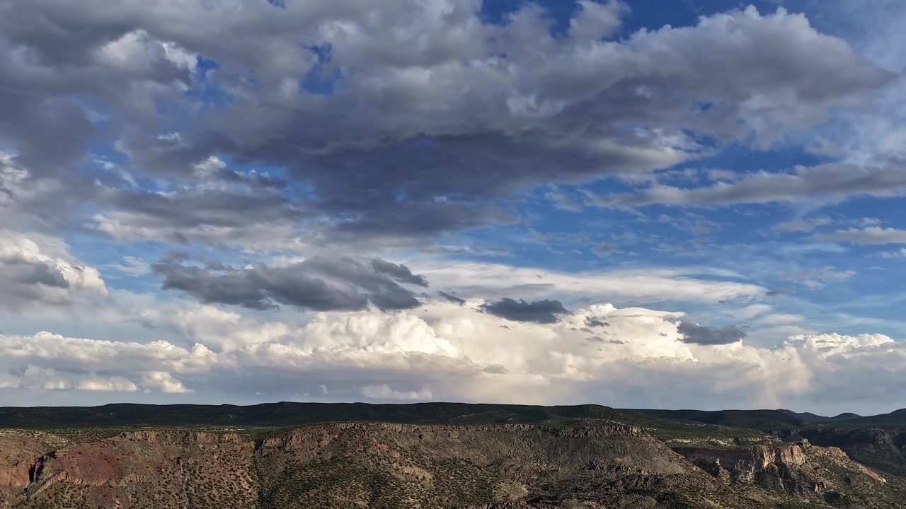 A sweeping 4K timelapse capturing fast-moving, multi-layered storm clouds rolling over a rugged desert canyon ridge. Dynamic shadows and shifting light reveal a beautifully wild, expansive landscape.