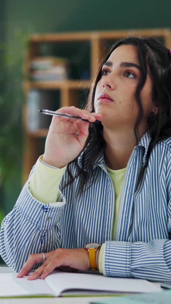 Giovane donna pensierosa seduta alla scrivania mentre scrive su un quaderno
