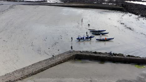 Drohnenprofilansicht-Von-Menschen,-Die-Currach-Boote-In-Richtung-Gewässerrand-Tragen