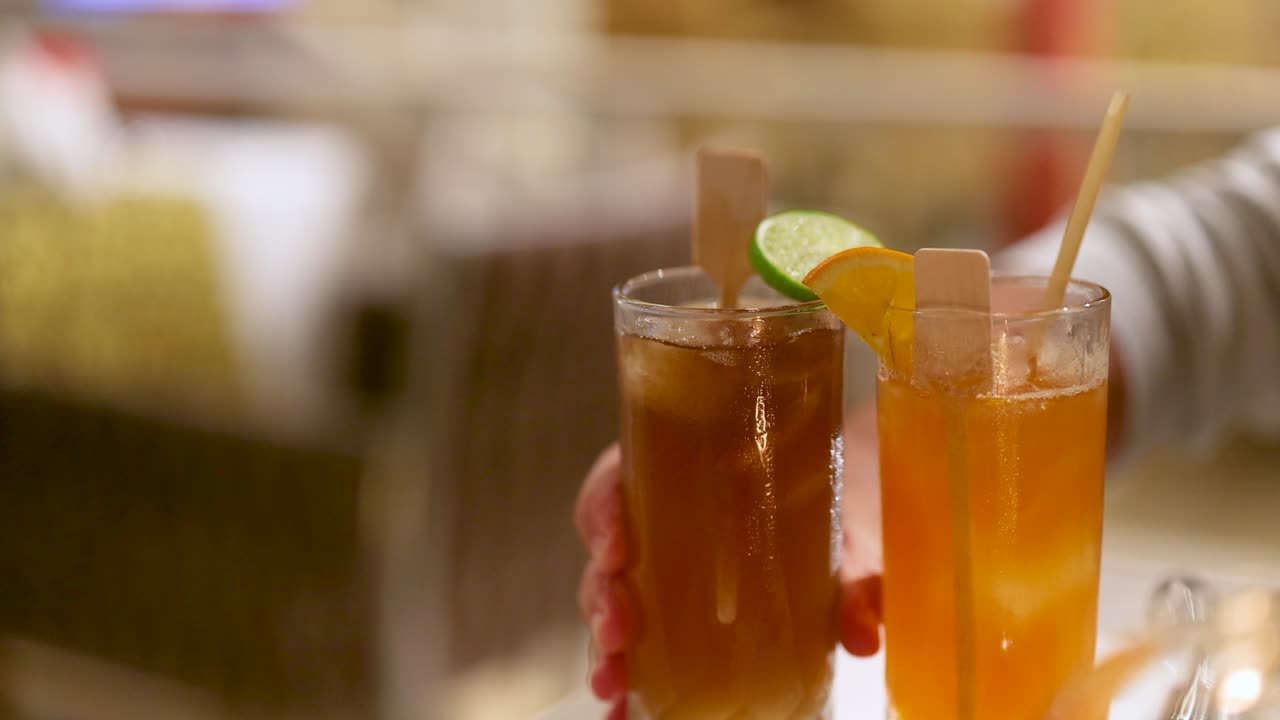 la mano sirviendo dos cócteles coloridos con guarniciones de frutas lentamente