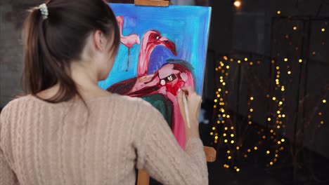 woman painting flamingos on canvas