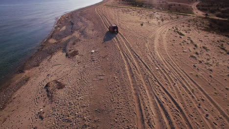 Aerial-View-car-driving-on-the-beach-in-greece-surrounded-by-blue-water