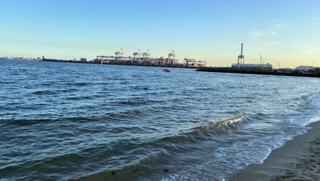 A-small-boat-moves-along-the-ocean-with-Port-Melbourne-docks-in-the-backdrop