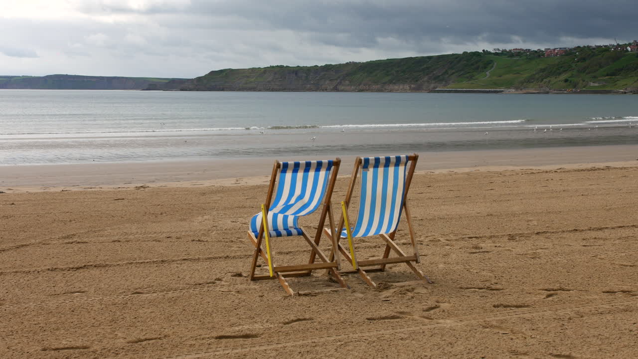 Fishing pots stacked near the water's edge with a lighthouse and moored boats visible across the harbor in Scarborough, North Yorkshire in England