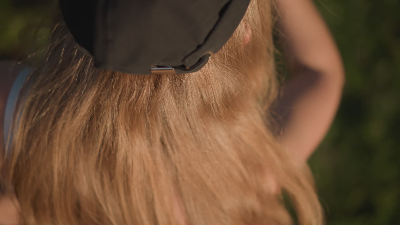 Portret van een Kaukasische danser in een zonnig park die knipogend wijst, close-up tijdens het gouden uur van bovenaf, roodblond haar onder een zwarte pet, sproetige huid die zonnestralen opvangt, speels gebaar naar de camera, energiek