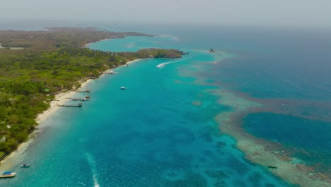 toma aérea de una isla en el océano rodeada de corales y barcos, colombia, cartagena