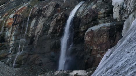 waterfall stream flowing from glacier along rocky wall