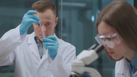 Hombres-Y-Mujeres-Científicos-Están-Trabajando-En-Laboratorios-Químicos-Investigando-Y-Experimentando-Con-Reactivos-Viendo-La-Reacción-Por-Microscopio