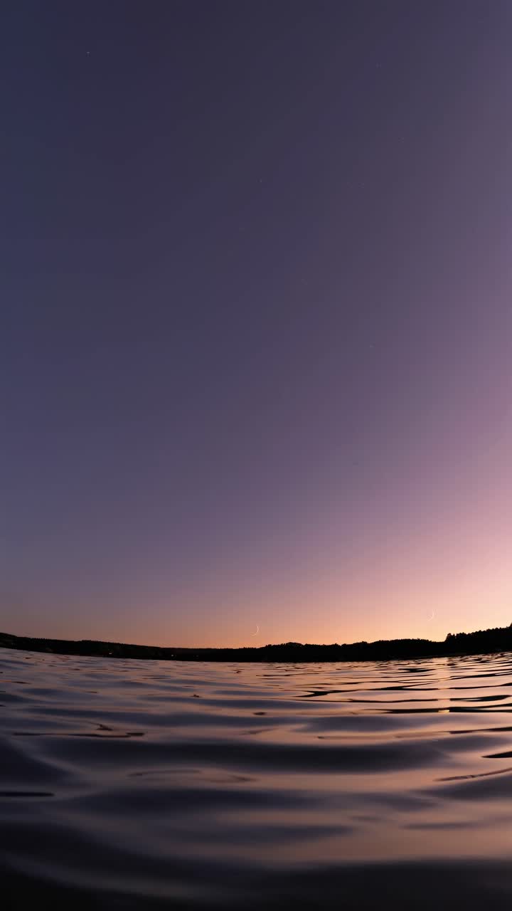 A serene sunset over a calm lake, captured from a low-angle perspective, ideal for a tranquil video