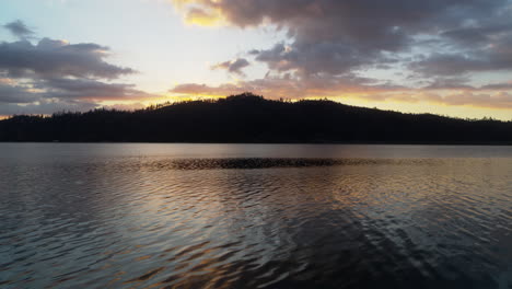 Close-aerial-flyover-of-the-waters-of-Whiskeytown-Lake-in-Northern-California-towards-a-sunrise-backlit-mountain