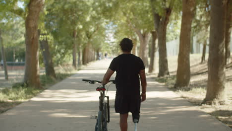 back view of man with bionic leg walking down alley with bike