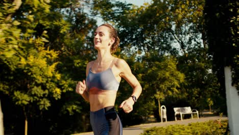 syomka cerca de una chica feliz en un uniforme de verano deportivo corre a través del parque de la mañana y mira su reloj. lograr sus registros y mejorar sus resultados