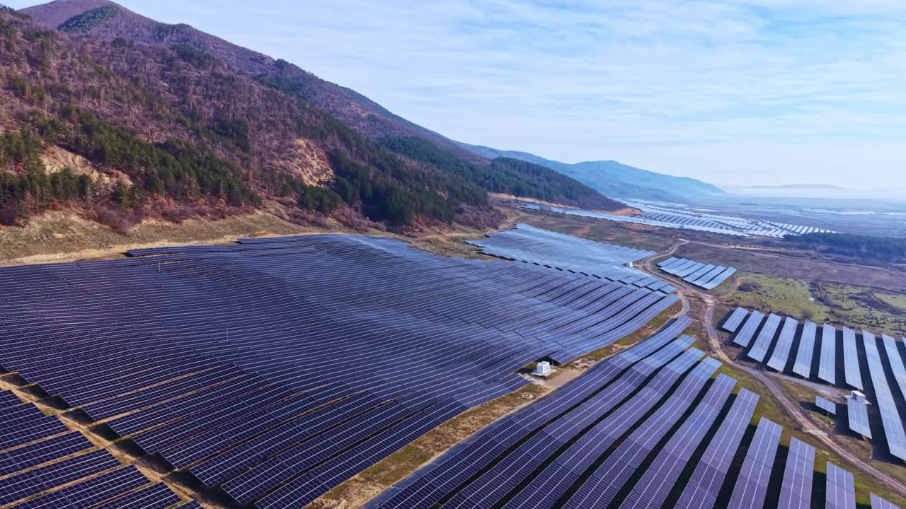 Solpaneler dækker et stort område i en dal omgivet af bjerge i dagtimerne i et vedvarende energiprojekt.