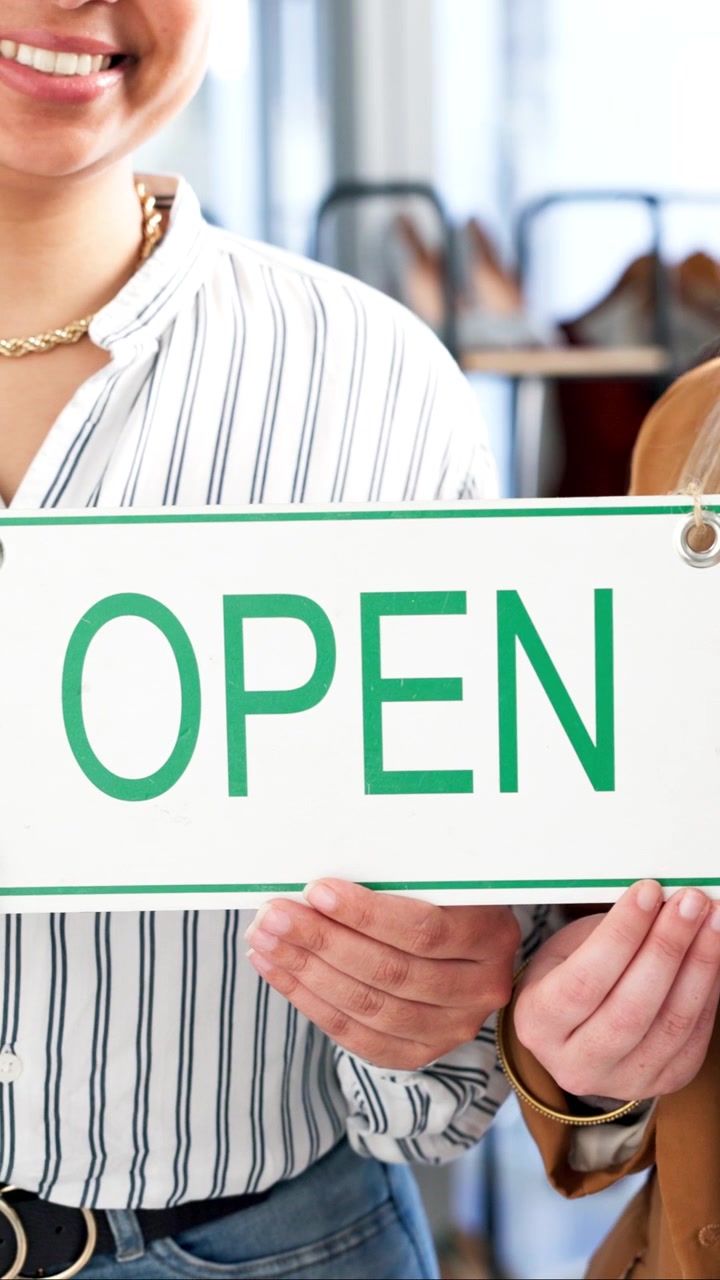 Two Women Holding an Open Sign in a Retail Store