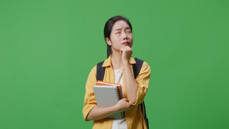 estudiante asiática con una mochila y algunos libros pensando y mirando a su alrededor luego levantando su dedo índice mientras estaba de pie en el estudio de fondo de la pantalla verde