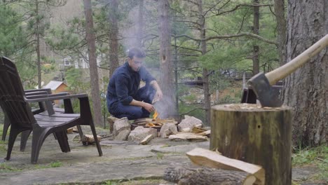 A-man-is-starting-a-fire-in-an-outdoor-fire-pit,-surrounded-by-trees