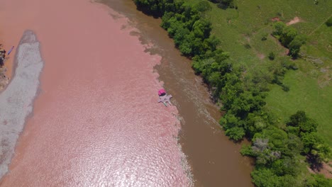 Native-people-on-a-boat-in-the-muddy-waters-of-oxapampa,-peru,-surrounded-by-lush-greenery,-aerial-view