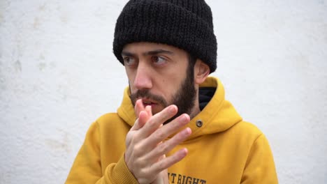 man in hipster beanie hat and yellow hoodie jacket rubbing hand palms and freezing in cold