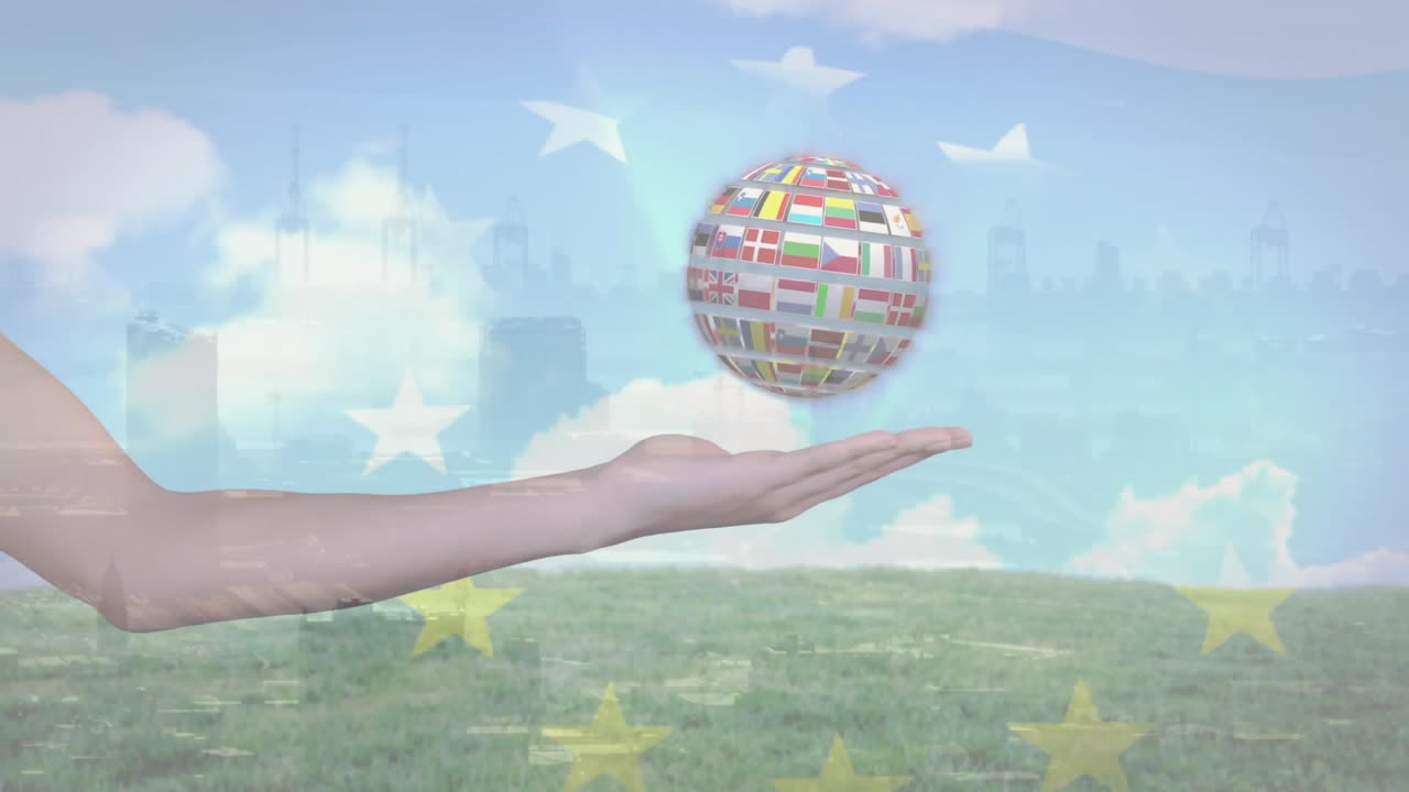 Holding globe with international flags, hand above grassy field and blue sky