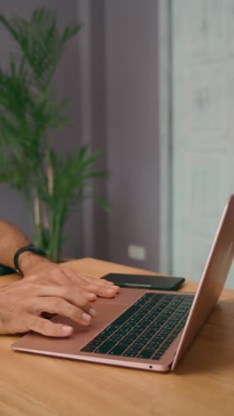 person working on a rose gold laptop at a wooden desk