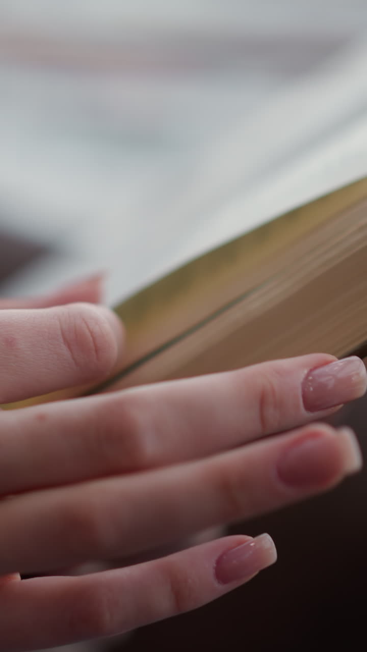 primer plano de la mano girando una página de un libro con ligero desenfocamiento, centrándose en el movimiento de la mano a medida que se voltea a la siguiente página mientras el libro permanece parcialmente fuera de enfoque
