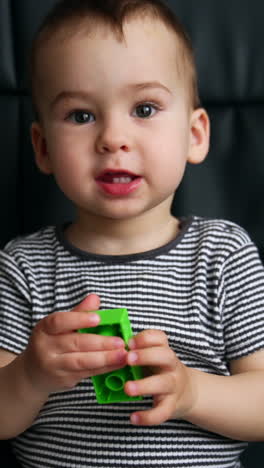 beautiful caucasian kid sits in a black office chair. cute child turns a piece of constructor and says something. vertical video