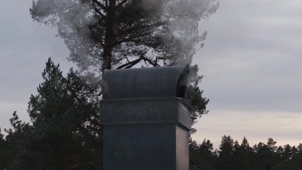 Røg stiger op fra en skorsten på et hytte tag mod en overskyet vinterhimmel. Roterende luftoptagelse.
