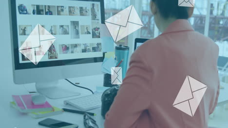 Animation-of-envelopes-over-biracial-female-photographer-looking-at-camera-while-working-in-office