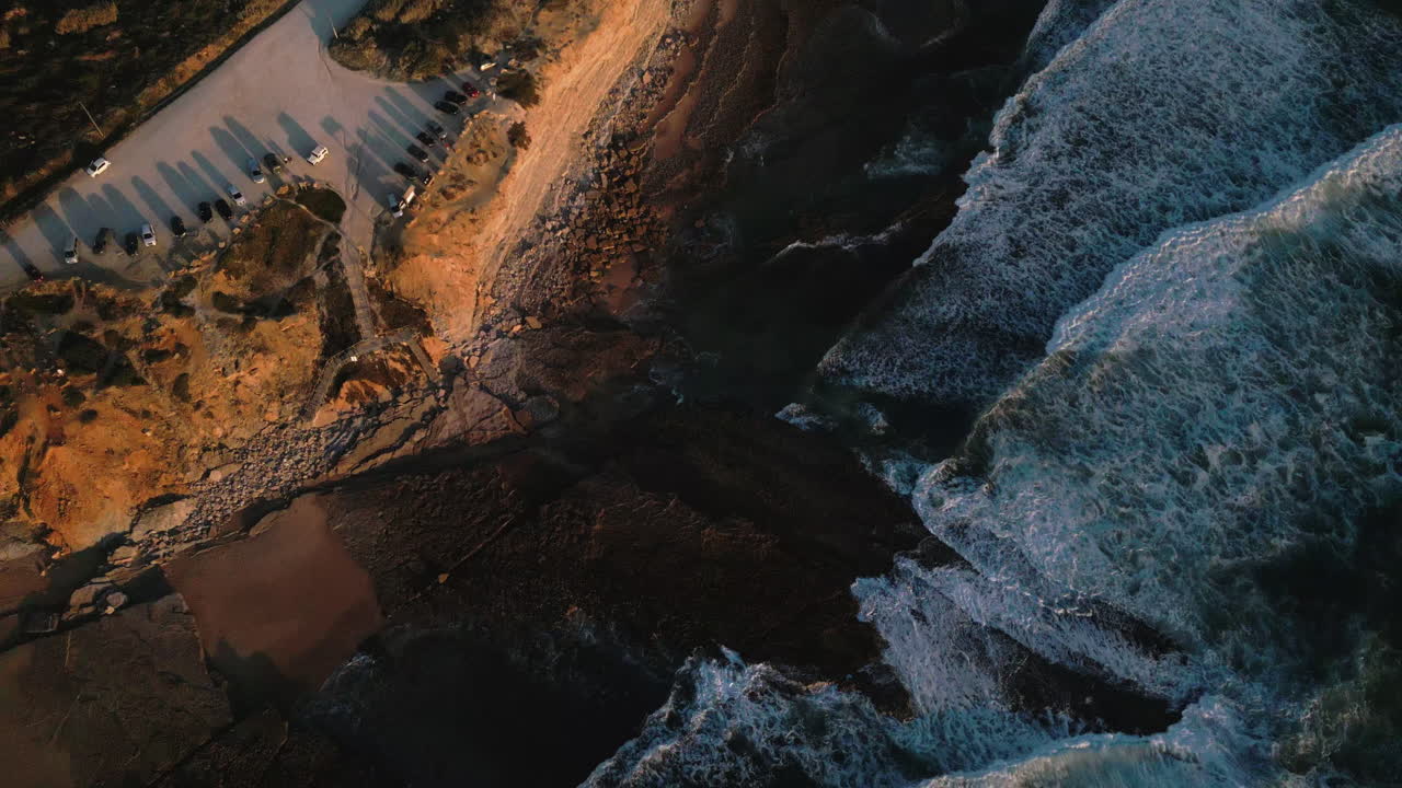 Top down drone shot of waves and coastline at sunset