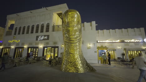the golden thumb monument in doha, qatar, lit up at night with people walking nearby