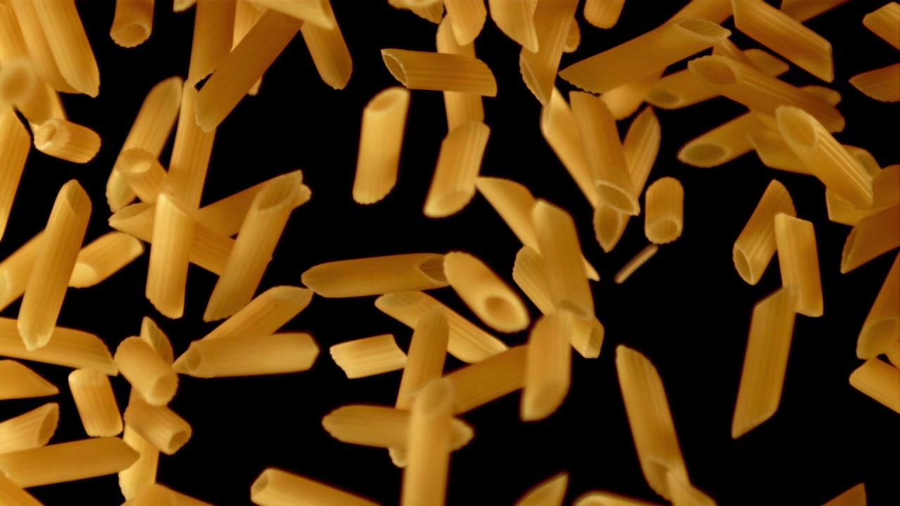 Pasta penne cruda che cade al rallentatore su sfondo nero