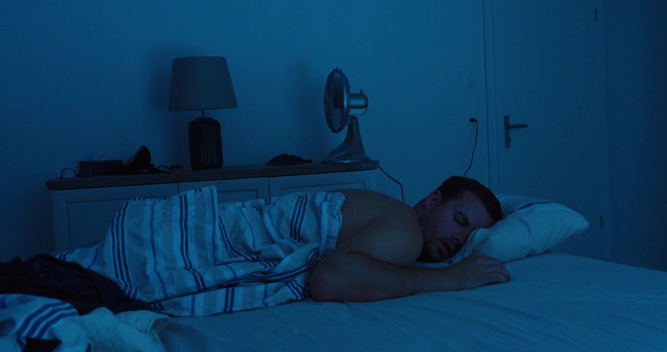 Un uomo dorme pacificamente con un ventilatore elettrico acceso in camera da letto durante una calda notte d'estate
