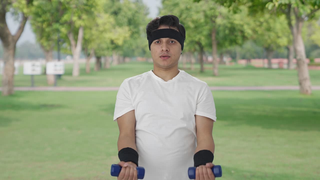 진지한 인도인 남자가 덤벨을 들어 올리고 있습니다.