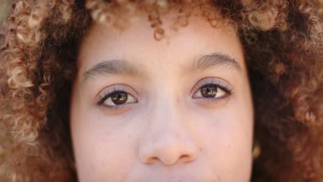 portrait of happy biracial woman with curly hair looking at camera in garden in slow motion