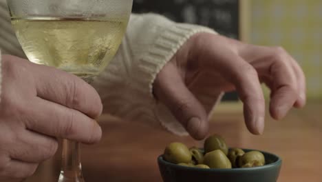 Hand-Mit-Einem-Glas-Weißwein,-Der-Oliven-Mit-Den-Fingern-Isst