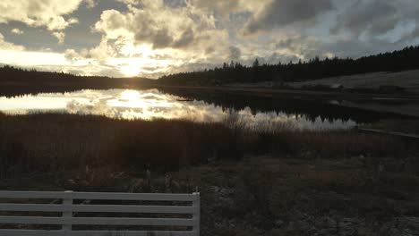 vista tranquila del lago de vislumbre durante la puesta de sol, un día nublado con vallas de rancho pintadas de blanco en la columbia británica, canadá