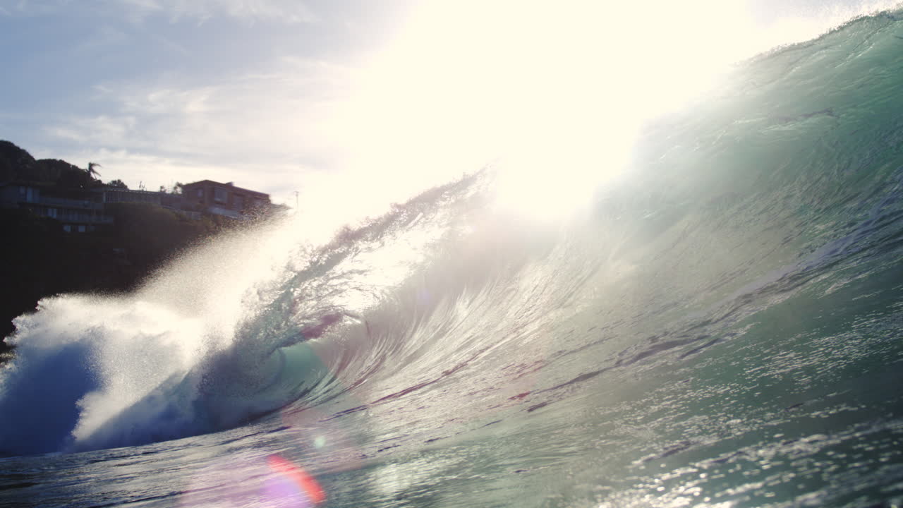 Backlit wave crashes in slow motion with glassy sunlit texture