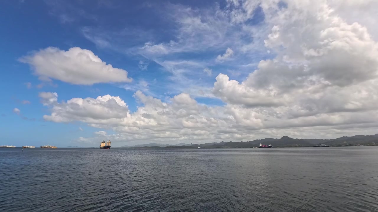 青空の下、船と遠くの山々が見える穏やかな海の広大な眺め。