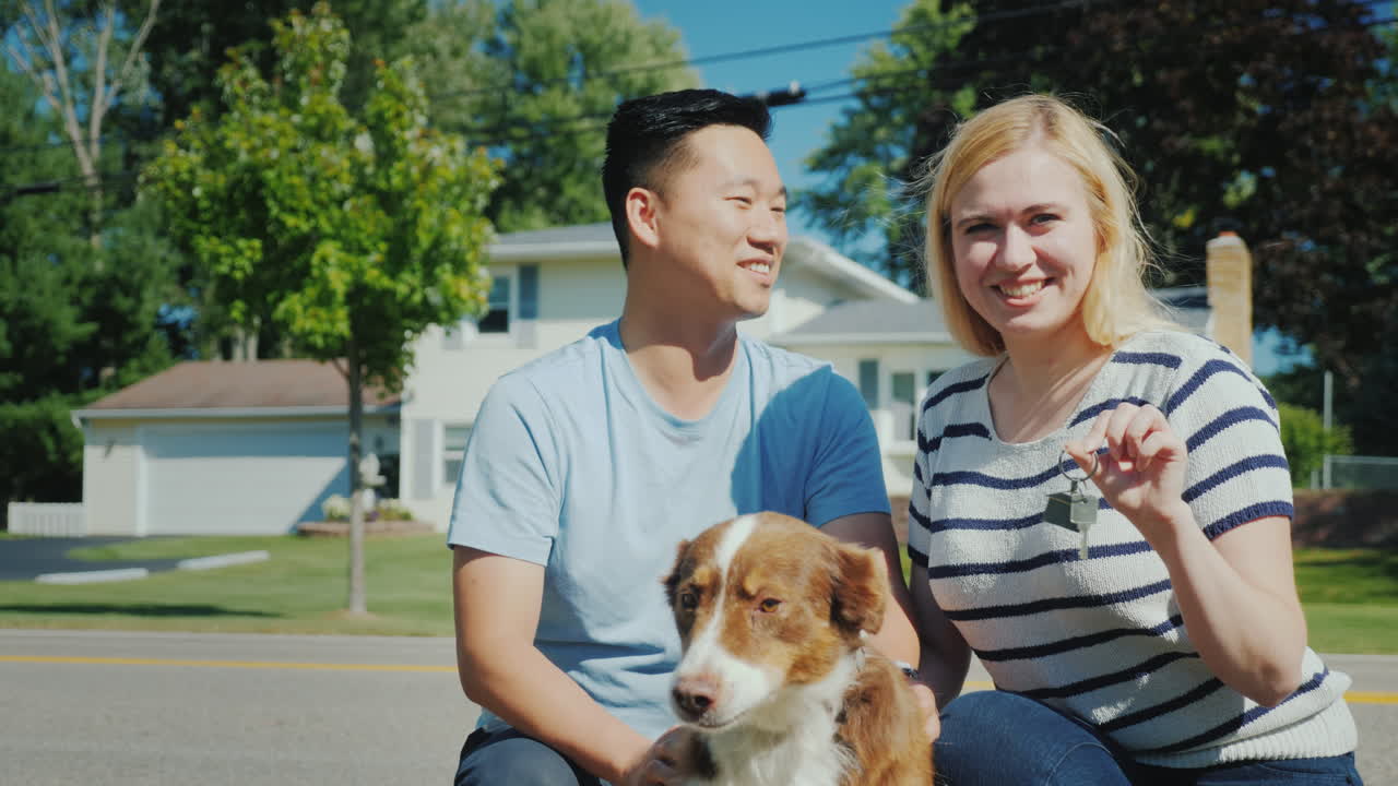 그들의 새 집 배경에 개가 있는 가족의 초상화 그들은 손에 열쇠를 쥐고 있다