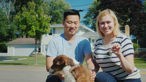 Portrait-Of-A-Family-With-A-Dog-On-The-Background-Of-Their-New-Home-They-Hold-The-Key-In-Their-Hands