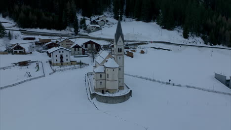 orbiting aerial view of snow-covered church building in the quaint village of trafoi beside the stelvio pass road