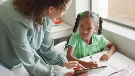 Video-of-happy-caucasian-female-teacher-explaining-lesson-on-tablet-to-african-american-girl