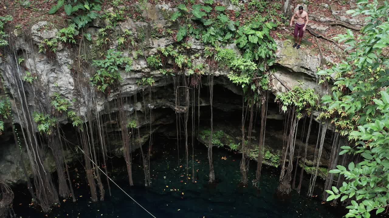 un hombre salta desde un alto acantilado a un cenote en méxico