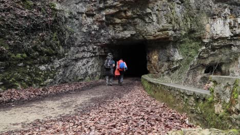 two backpackers hiking into a tunnel in a mountain outdoors