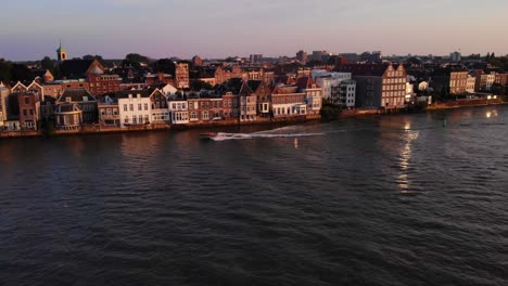 Boat-Speeds-Down-The-River-Near-The-Cityscape-Of-Dordrecht-In-Netherlands