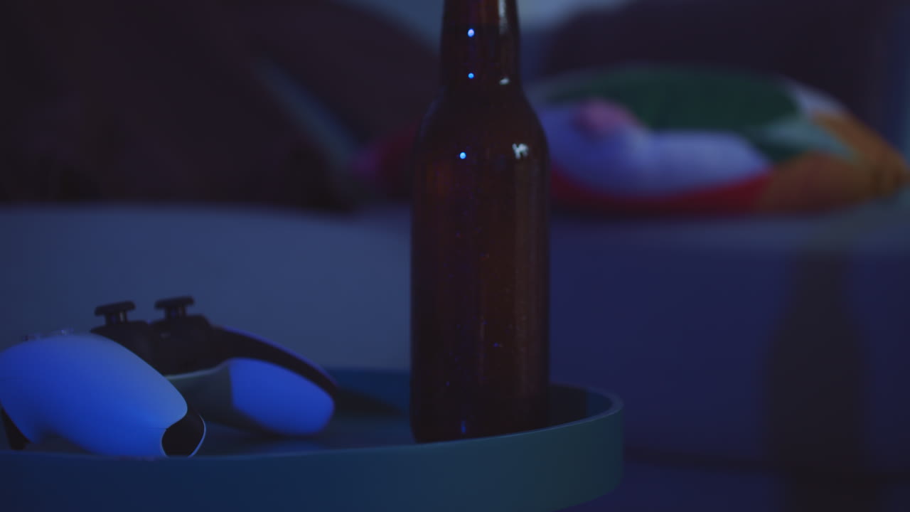 Game night with console controller and bottle of beer inside cozy room, handheld shot