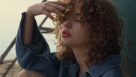 Gentle-woman-sitting-beach-leaning-on-old-boat-close-up.-Curly-model-posing.