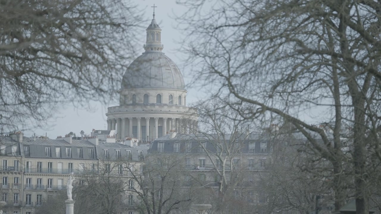 La cupola del Pantheon si erge sopra alberi invernali spogli e una statua da giardino nel centro di Parigi.