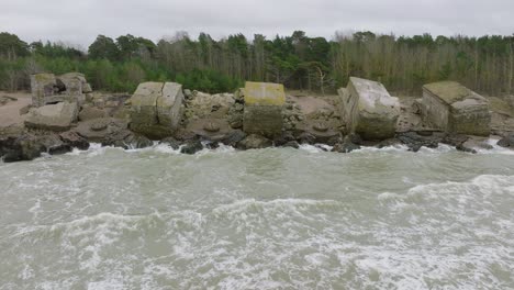 Aerial-establishing-view-of-abandoned-seaside-fortification-buildings-at-Karosta-Northern-Forts,-Baltic-sea-coast-,-large-waves,-overcast-day,-slow-motion,-drone-dolly-shot-right